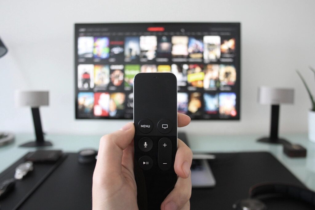 Hand holding a streaming remote in front of a TV showing a grid of apps