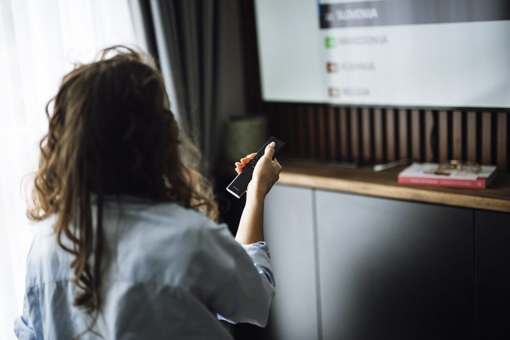 Person holding a remote control in front of a smart TV showing a channel menu